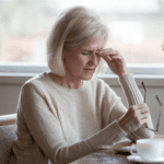 Middle aged woman, sat at a table, removed glasses, rubbing eyes, dry eye, glaucoma
